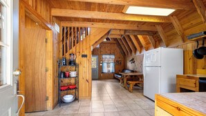 Ein Holzinnenraum mit Küchenbereich, der einen weißen Kühlschrank, hölzerne Regale mit Geschirr und einen Esstisch zeigt.