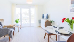 A bright living room with a dining area, a TV, and a balcony with plants.