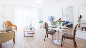 A modern living room with a dining table, chairs, and a TV. There is a sofa and a coffee table with decorative items.