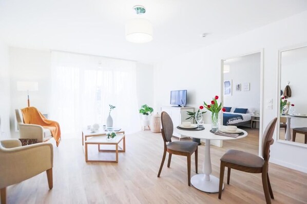 Una sala de estar moderna con una mesa de comedor, sillas y una televisión. Hay un sofá y una mesa de centro con objetos decorativos.