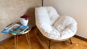A white cushioned chair with a round table beside it, a white vase with a plant, and a magazine on the table. - Villa 'Giovanna' with Private Pool, Wi-Fi and Air Conditioning (sorso)