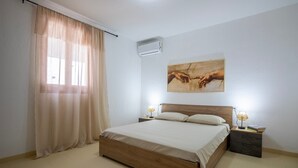A bedroom with a wooden bed, beige curtains, an air conditioner, a nightstand with a lamp, and a painting on the wall. - Villa 'Giovanna' with Private Pool, Wi-Fi and Air Conditioning (sorso)