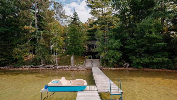A wooden dock extending into a clear lake, with a small boat docked at the end. - Lakeside Escape | 5BR | Hot Tub | Family Friendly (Traverse City)