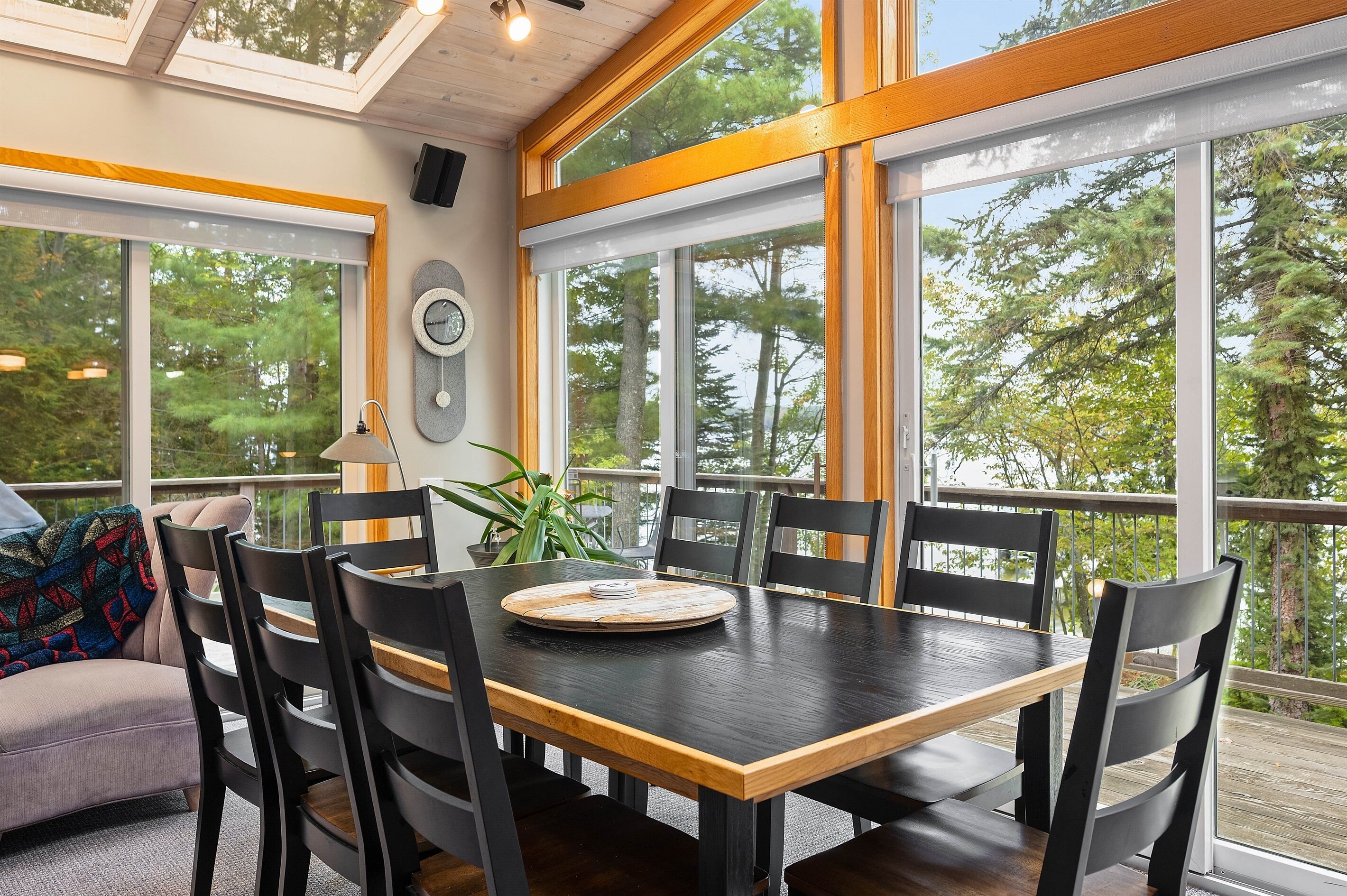 A dining area with a wooden table and chairs, large windows with a view of trees, and a ceiling with skylights.
