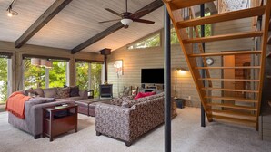 A spacious living area with a large sofa, a coffee table, and a fireplace. There is a wooden staircase and a TV mounted on the wall. - Lakeside Escape | 5BR | Hot Tub | Family Friendly (Traverse City)