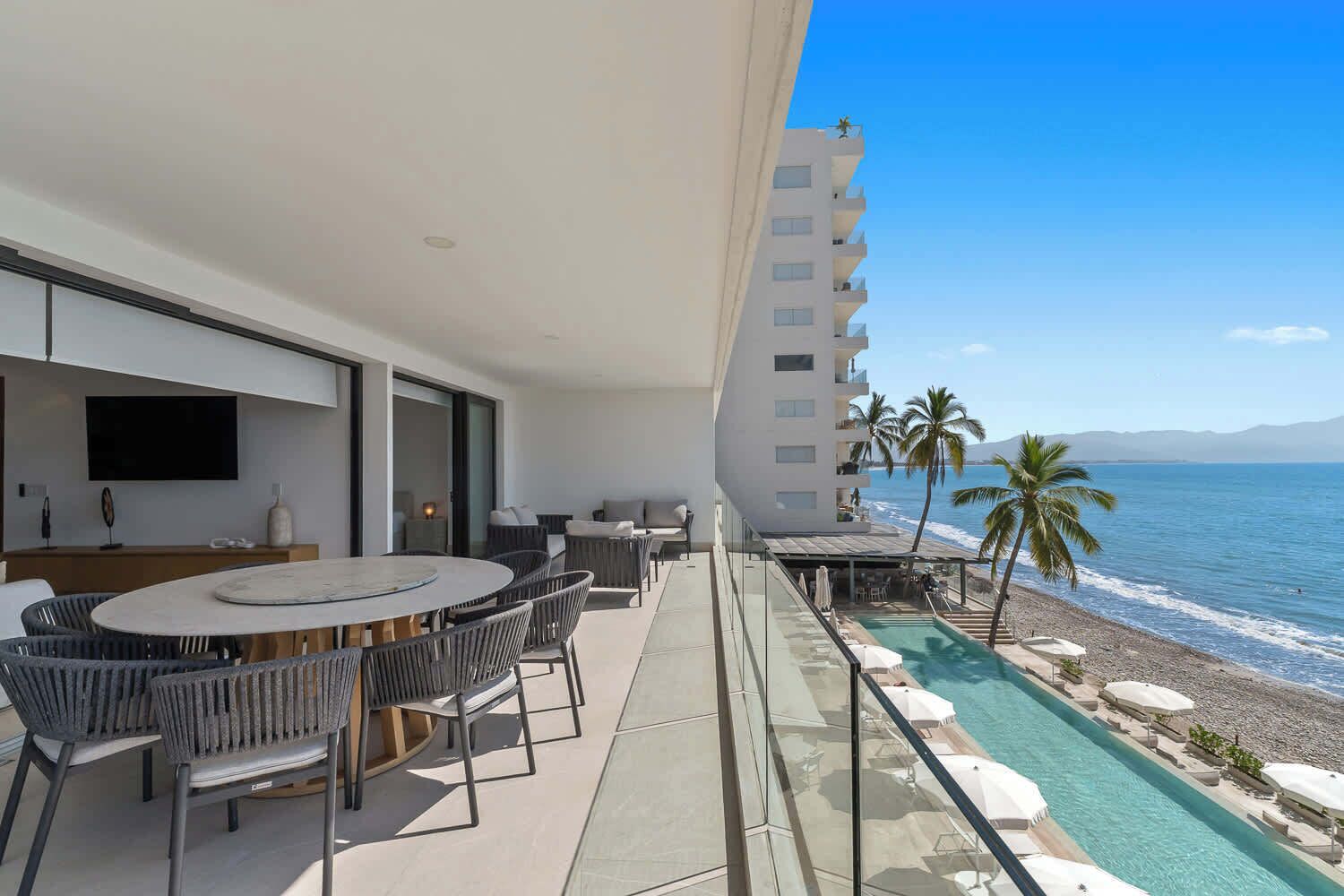 A balcony with a dining area, a pool, and a view of the ocean.