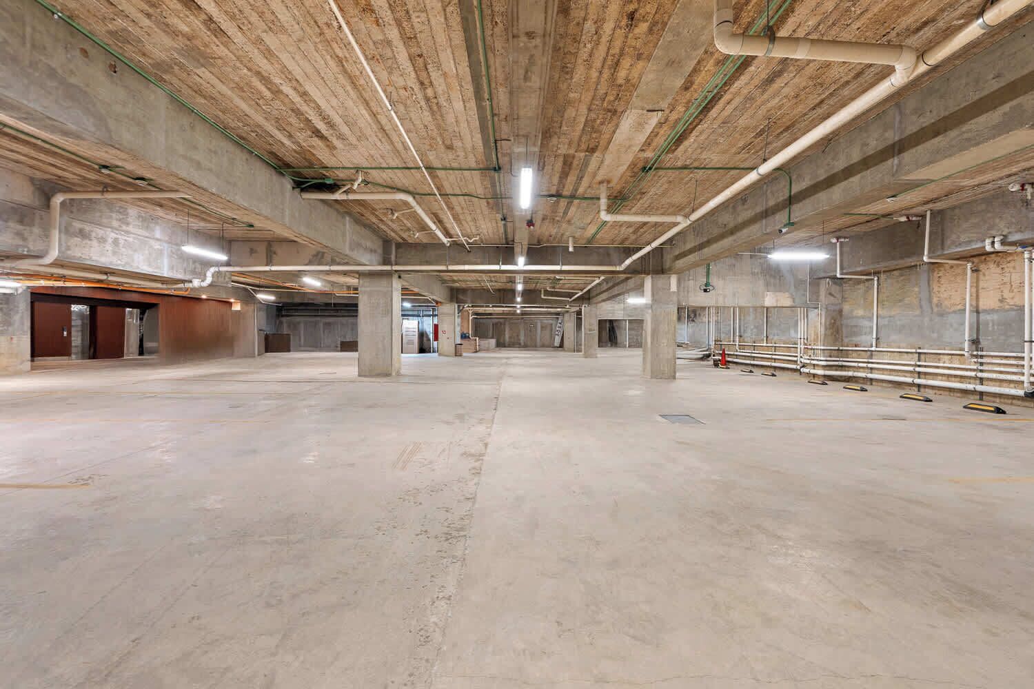 A spacious indoor area with concrete floors and ceiling, visible structural beams, and exposed ductwork.