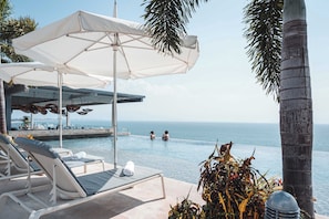 A pool area with lounge chairs, umbrellas, and a view of the sea.