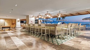 Un vaste espace de restauration intérieur, avec une longue table et des chaises, un comptoir de bar et une vue sur l’océan.