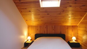 A bedroom with a wooden ceiling, a bed, two bedside tables with lamps, and a skylight.