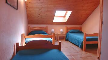 Quarto com duas camas de madeira, um claraboia e piso ladrilhado.