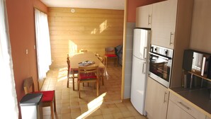 A kitchen with wooden cabinets, a refrigerator, and a dining area with chairs and a table.