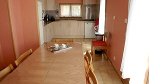 A compact kitchen with white cabinets, a wooden dining table, and a red chair.