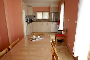Une cuisine de taille réduite avec des meubles blancs, une table à manger en bois et une chaise rouge.