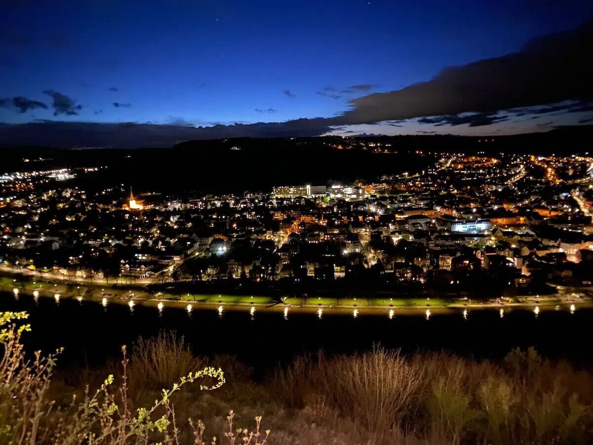 A nighttime cityscape with a river in the foreground and a mountain range in the background.