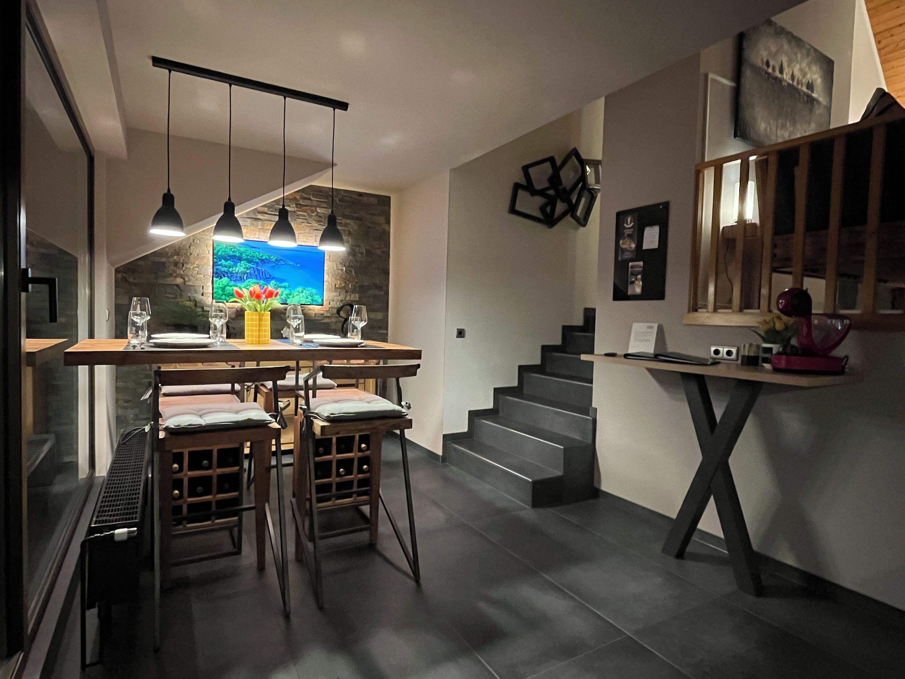 Een moderne keuken met een eetgedeelte, voorzien van een stenen spatwand, hanglampen en een grote flatscreen-tv.