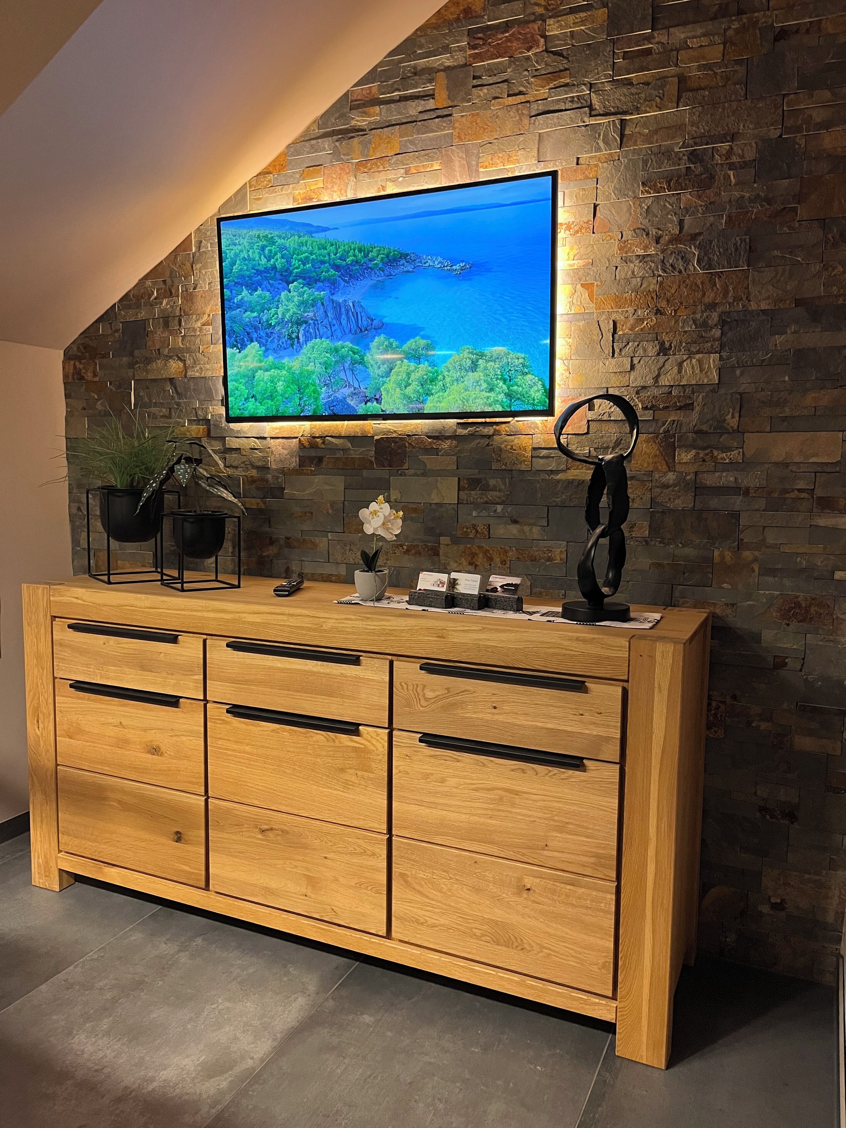 Een houten kast met meerdere lades en een flatscreen televisie die aan een stenen muur is bevestigd.