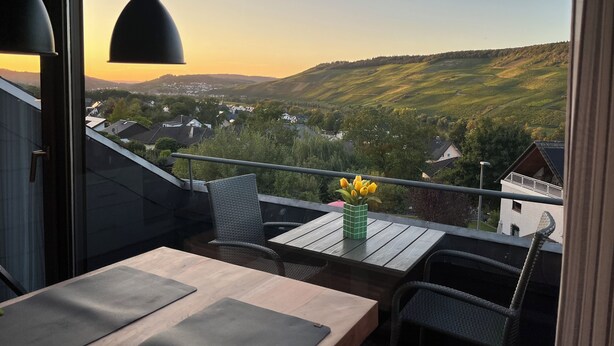 Un balcone con tavolo e sedie, affacciato su un panorama pittoresco di una valle con case e vegetazione.