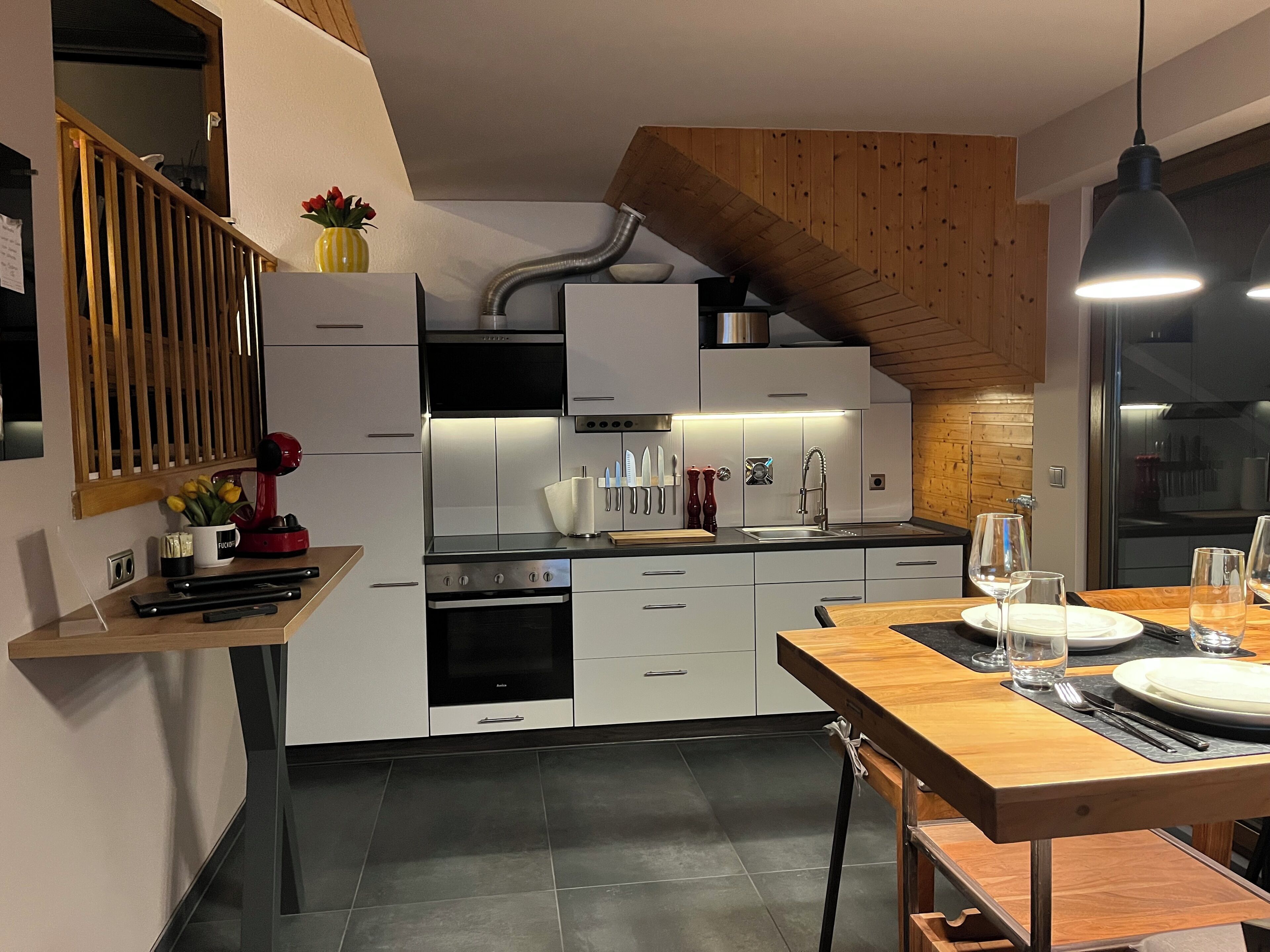 A modern kitchen with white cabinets, a wooden ceiling, and a dining area with a wooden table and chairs.