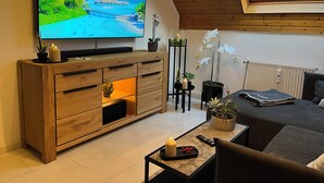 Un soggiorno moderno con una TV su un mobile in legno, un divano, un tavolino da caffè con una candela e un'orchidea in vaso.