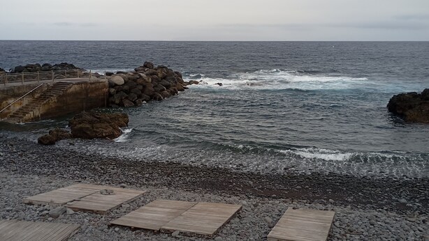 A rocky beach with a concrete walkway leading to a wooden deck.