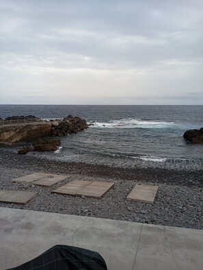 A rocky beach with a concrete walkway leading to a wooden deck.
