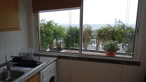 A kitchen with a washing machine, a sink, and a window with a view of trees and the sea.