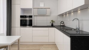 A modern kitchen with white cabinetry, a built-in oven, a stainless steel sink, and a black countertop. - AS HOME Kościuszki 89 (Wrocław)