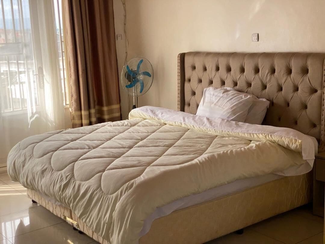 A bed with a quilted headboard, a bedside fan, and a window with curtains.