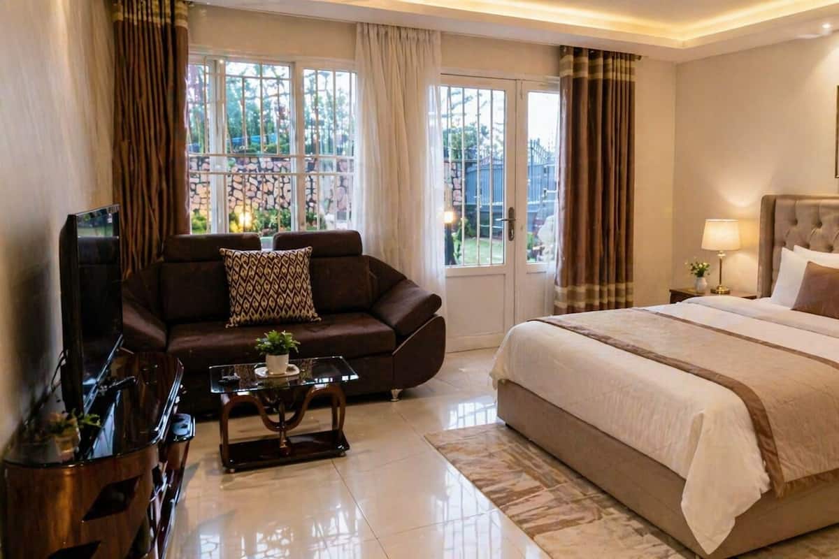 Ein Hotelzimmer mit einem großen Bett, einer Couch, einem Couchtisch, einem Fernseher und einem Fenster mit Vorhängen.