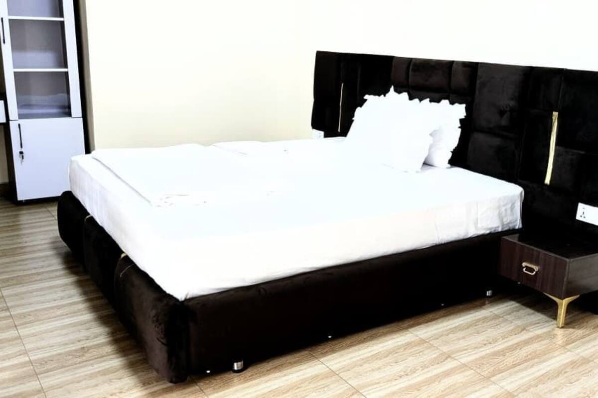 Ein Bett mit schwarzem Kopfteil und weißer Matratze in einem Zimmer mit Holzboden.