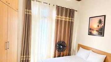 A bedroom with a bed, a nightstand, a fan, and a wooden wardrobe.