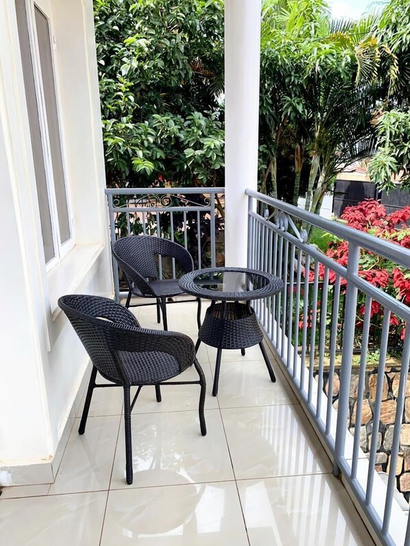 Un balcon agrémenté de deux fauteuils en osier et d’une petite table ronde, le tout entouré d’une rambarde en métal et de plantes en pot.