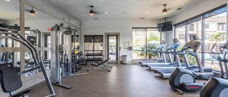 Un gimnasio con cintas de correr, máquinas de pesas y una pared de espejos.