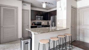 A modern kitchen with granite countertops, stainless steel appliances, and a bar area with stools.