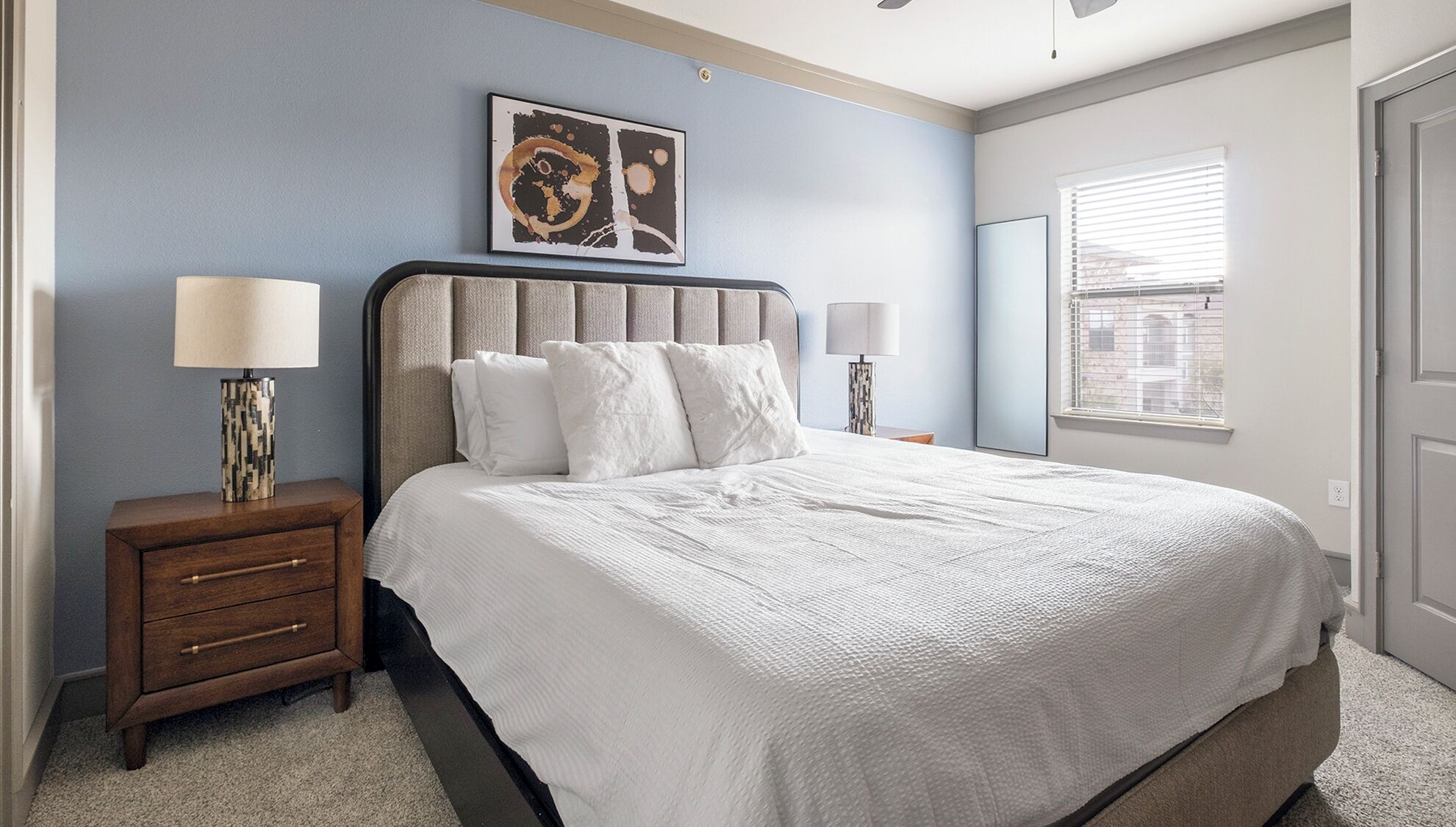 A bedroom with a large bed, two bedside tables, a wall-mounted artwork, and a window with blinds.