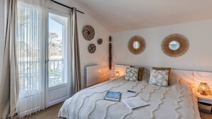 A bedroom with a bed, a window with curtains, a radiator, and wall decorations. - Eleuthera Guest Room with Lake View, Shared Pool and Wi-Fi (Gujan-Mestras)
