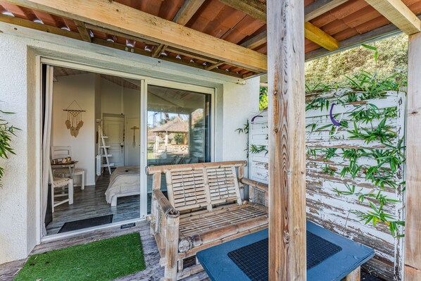 A wooden bench outside a room with a door, a small table, and a bamboo plant wall.