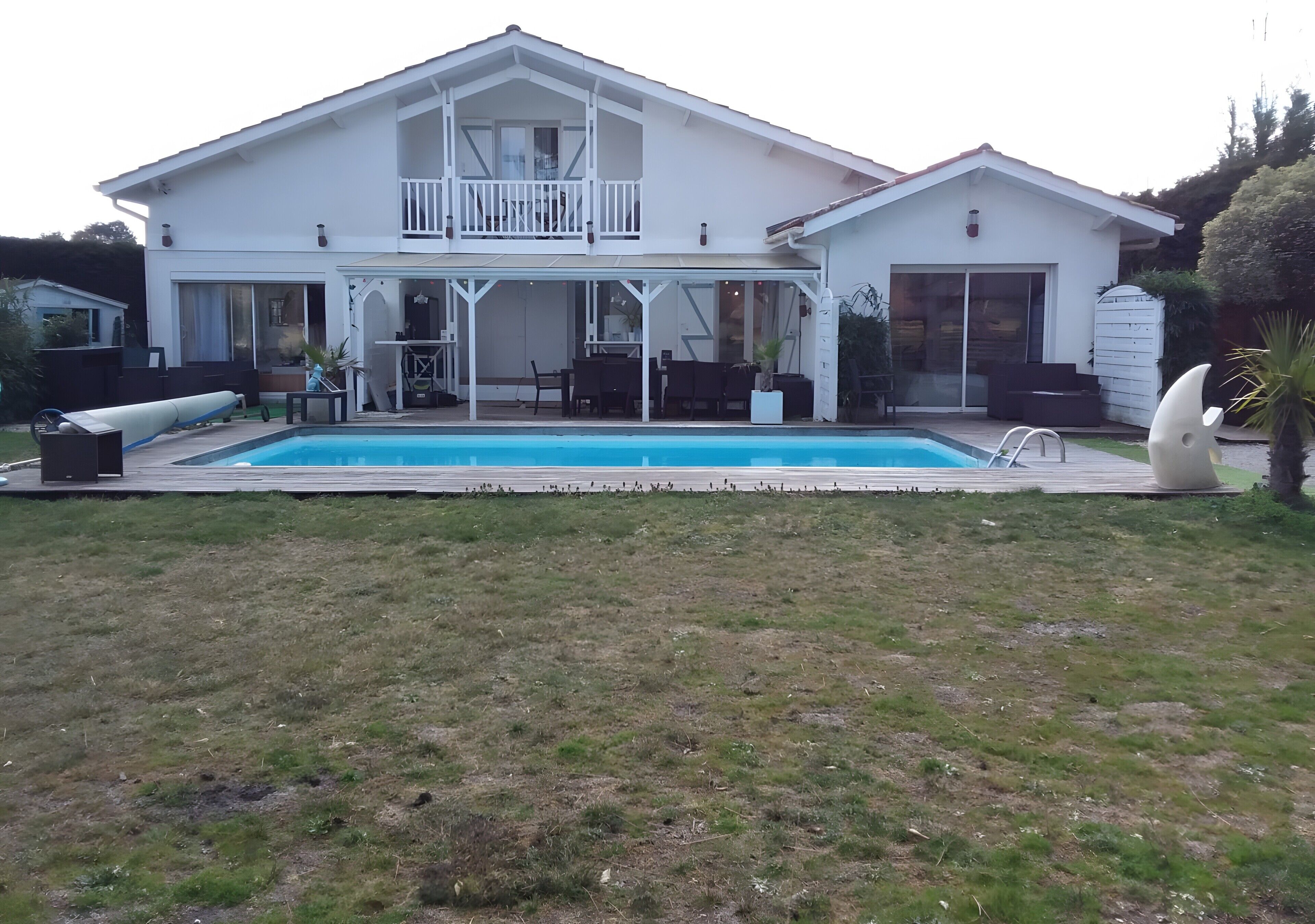 A two-story house with a balcony, a swimming pool, and outdoor furniture.
