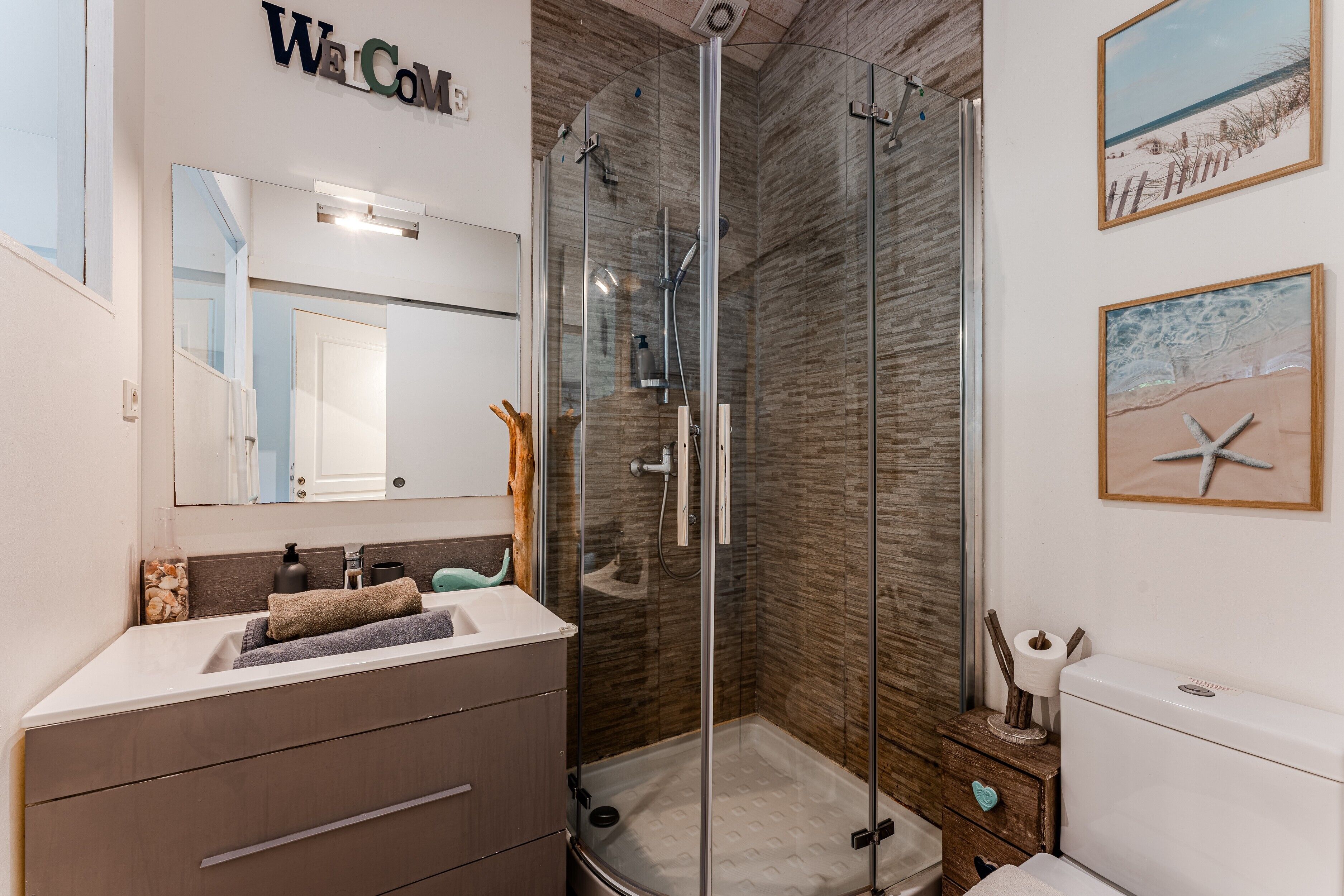 A modern bathroom with a glass shower enclosure, a sink with a towel, and a toilet.