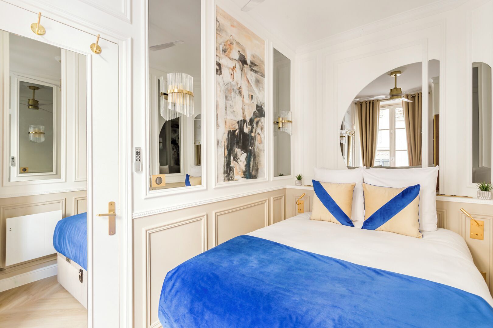 A bedroom with a large bed, a mirror, a painting, and a chandelier.