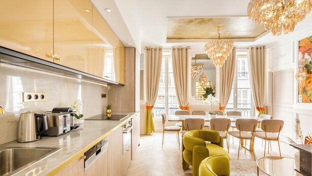Una cucina moderna con isola centrale, elettrodomestici integrati e zona pranzo con sedie gialle e tavolo in vetro.