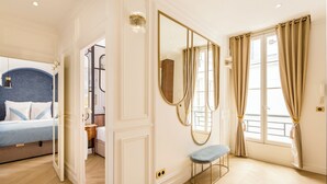Una camera d'albergo con un letto, una panca, uno specchio e una finestra con tende.