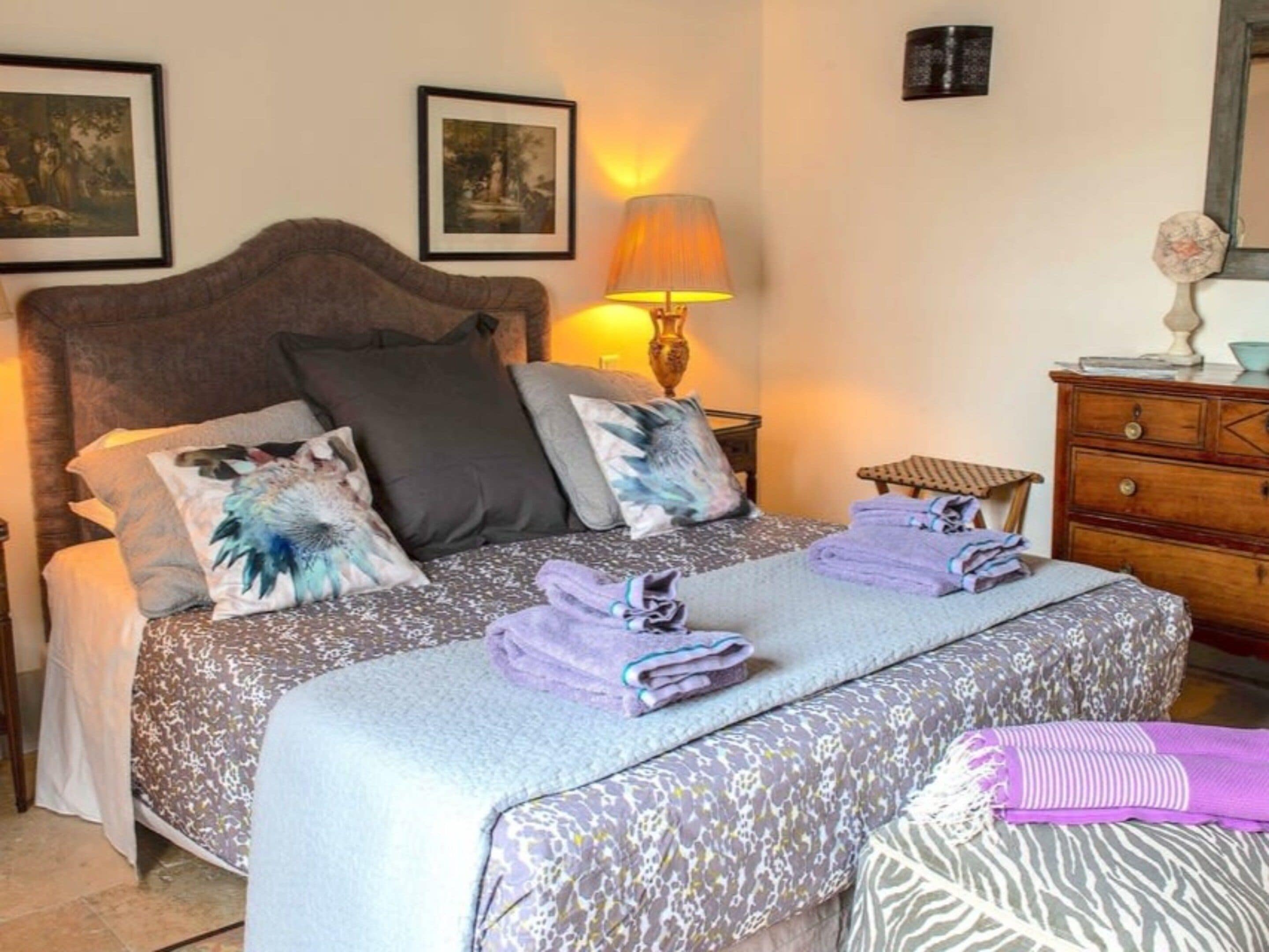 A neatly made bed with a patterned bedspread, pillows, and folded towels.