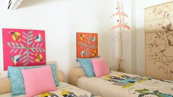 A bedroom with two beds, each with a colorful bedspread and pillows, a wooden dresser with floral patterns, and wall art depicting birds and flowers.