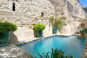 A stone building with a pool, potted plants, and a small window. - Heated Pool Apartment in Uzes (Uzès)