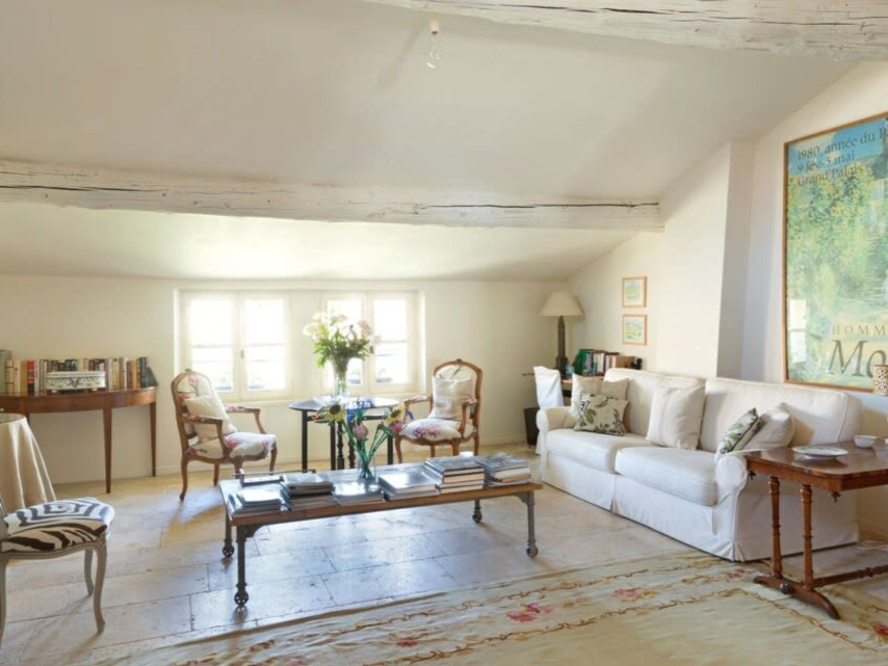 Un salón espacioso con un sofá blanco, una mesa de centro y una estantería. Una ventana grande ofrece luz natural.