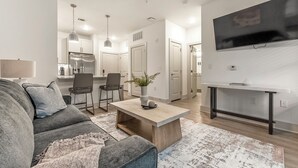 Een moderne woonkamer met een grijze bank, een salontafel en een aan de muur bevestigde televisie.