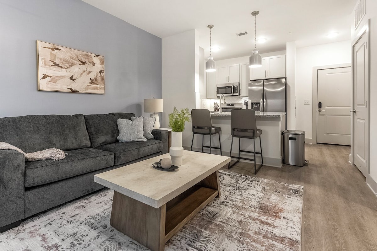 Ein modernes Wohnzimmer mit einem grauen Sofa, einem Holztisch und einem gemusterten Teppich.