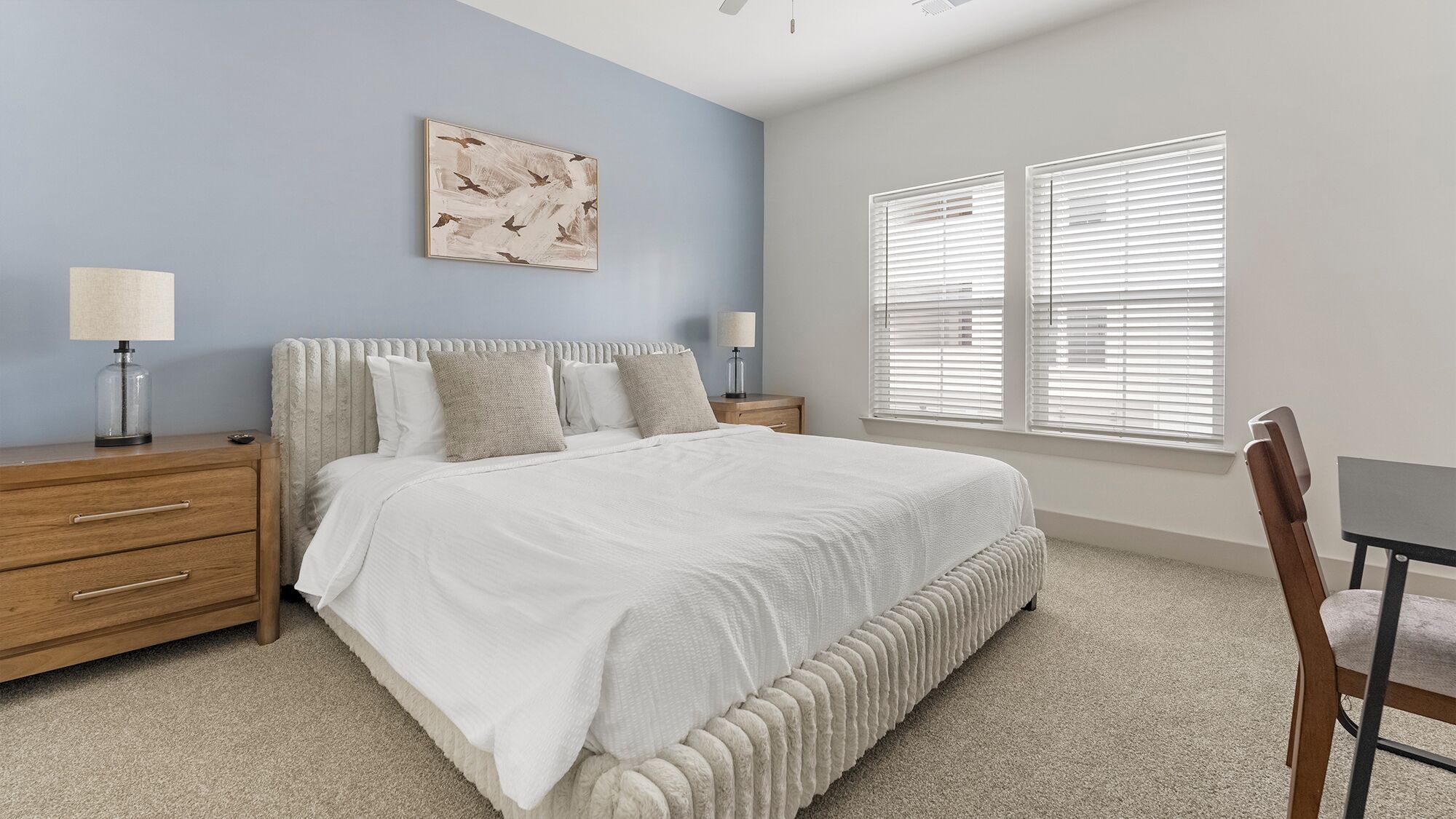 A bedroom with a bed, two bedside tables, a nightstand, a chair, and a window with blinds.